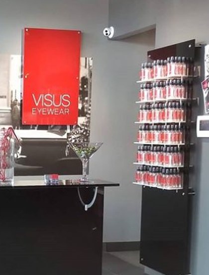 The Visus Eyewear reception counter, with the store's own red sign on the wall and a contact lens display beside it